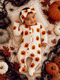 Smiling baby in a pumpkin-patterned onesie with a matching headband, surrounded by fall decorations.