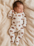 Infant asleep on a soft blanket, wearing a zip-up onesie with a bison pattern in earthy tones.