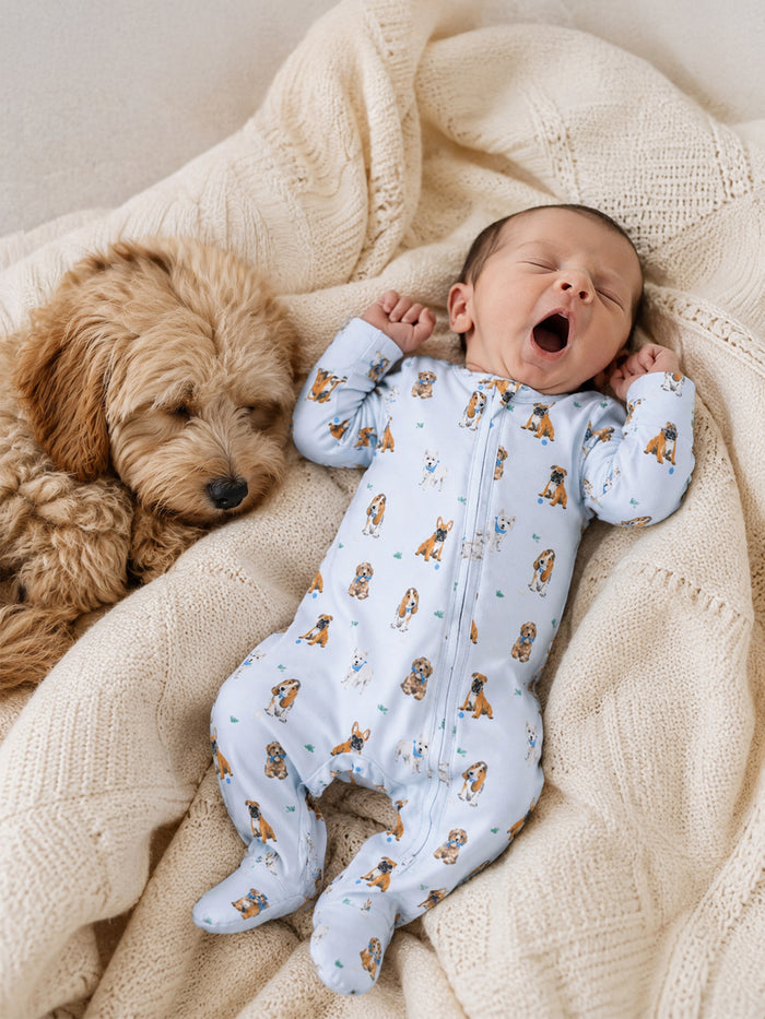 Baby in dog-print pajamas yawns beside a sleeping dog on a cozy blanket.