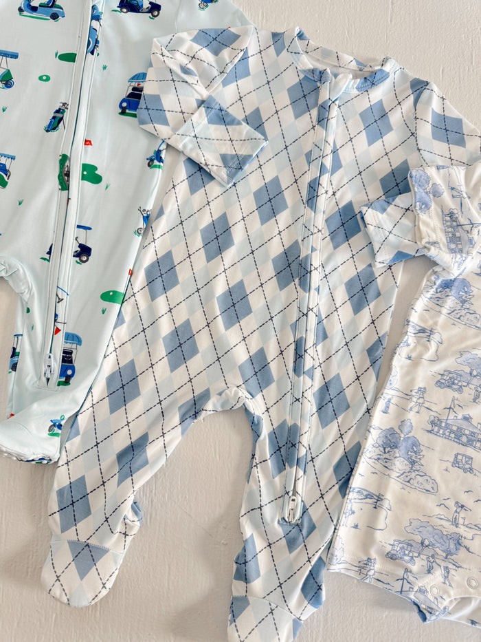 Three children's sleepers in blue patterns: one with trucks, one with argyle, and one with a light print.