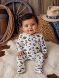 Smiling baby in a cowboy-themed outfit, sitting on a fluffy blanket with rustic decor in the background.