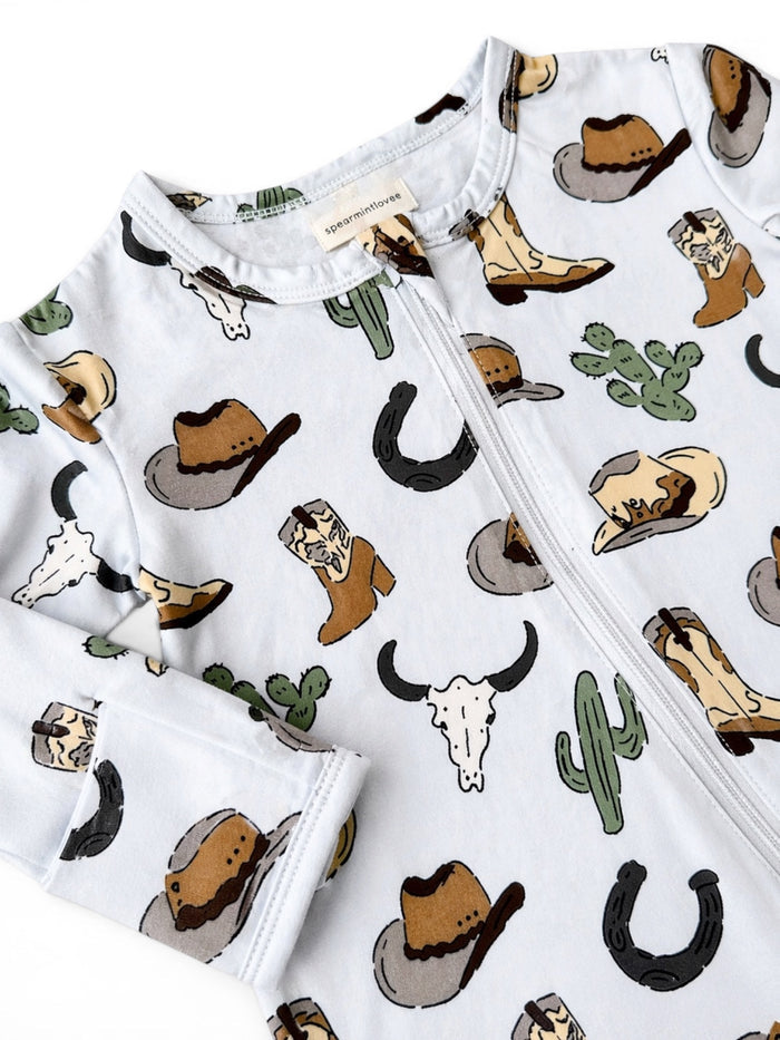 Cowboy-themed baby onesie featuring hats, boots, cacti, and western motifs on a light background.