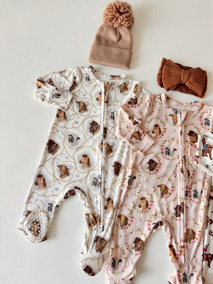 Baby clothes including animal print onesies, a brown pom-pom hat, and a brown headband on a white background.
