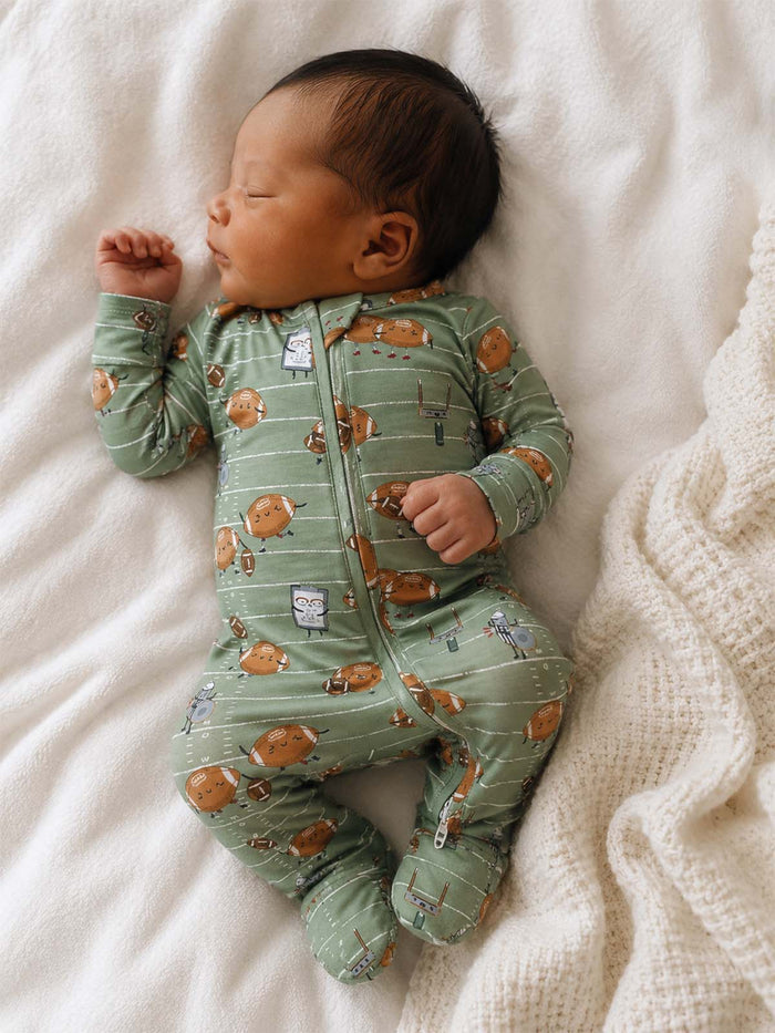 Newborn sleeping on a white blanket, wearing a green onesie with a playful animal print.
