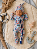 Sleeping baby in nautical-themed outfit on a cozy blanket, surrounded by decorative seashells and anchors.
