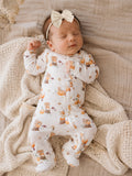 Baby wearing a pumpkin-patterned onesie and bow, peacefully sleeping on a textured blanket.