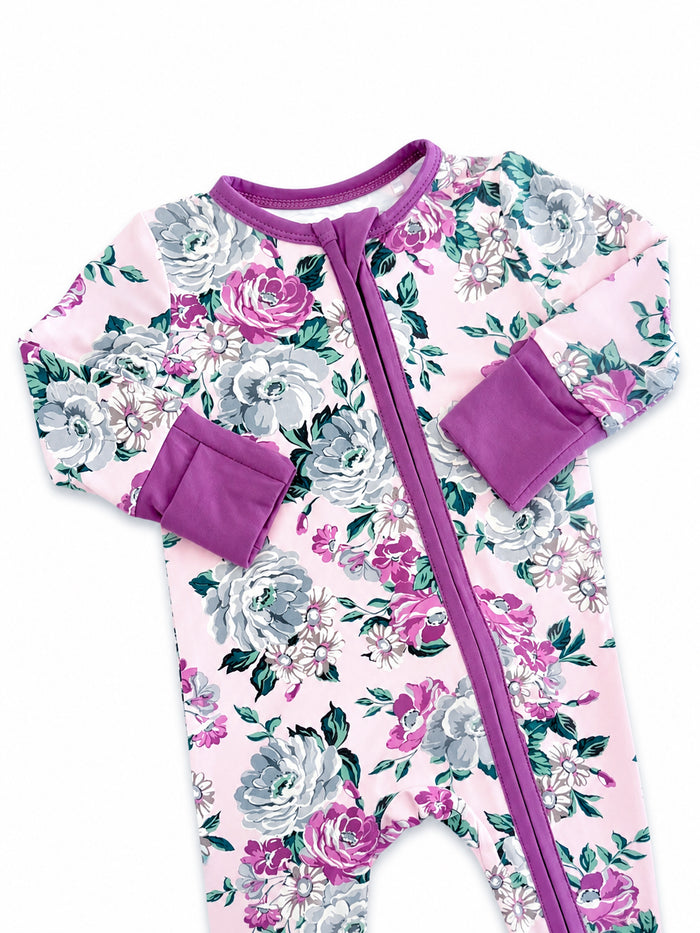 Floral infant onesie in pink with gray and purple flowers, featuring long sleeves and a front zipper.