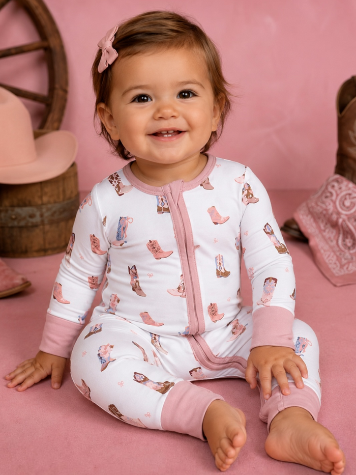 Smiling baby in a pink-themed room, wearing a cute cowgirl-themed onesie.