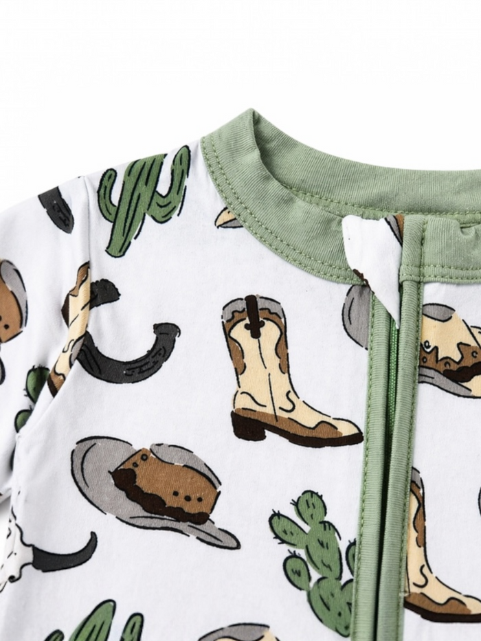 White fabric onesie featuring cowboy hats, boots, and cacti designs, with a green collar and front zipper.