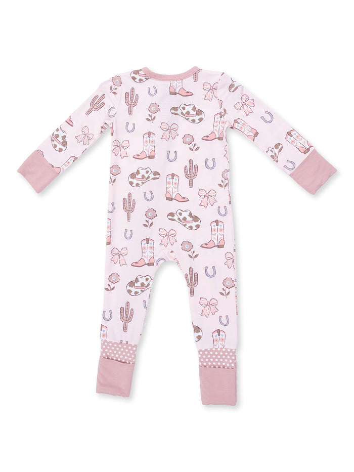 Pink baby onesie with cowboy-themed patterns like boots, cacti, and bows, featuring long sleeves and polka dot cuffs.