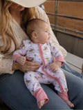 Mom holds a baby wearing a cute patterned onesie, sitting outdoors by a railing with a soft focus background.