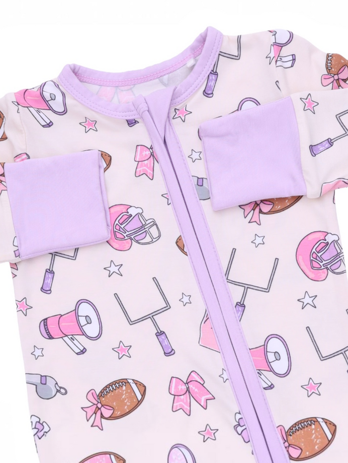 Light pink toddler onesie decorated with football, cheer, and star patterns, featuring purple accents and a front zipper.