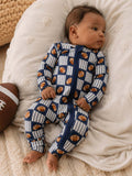 Baby in blue football-patterned onesie, lying on a soft blanket with a football nearby.