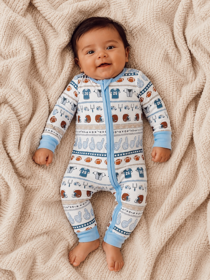 Smiling baby in a sporty onesie on a cozy blanket, surrounded by playful football-themed patterns.