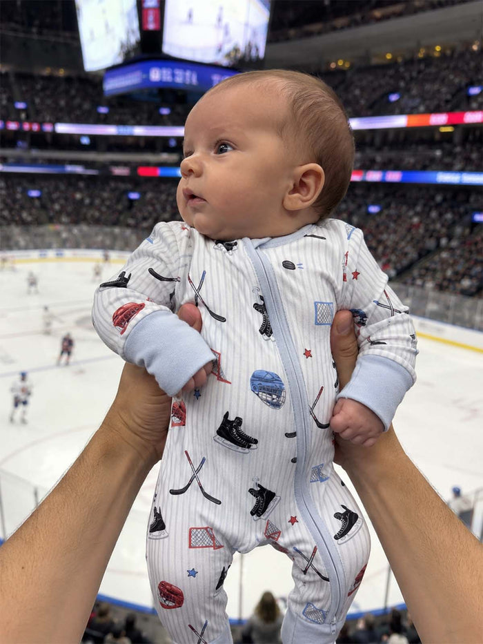 Baby in hockey-themed onesie held above a crowd at an ice hockey game, focused on their curious expression.
