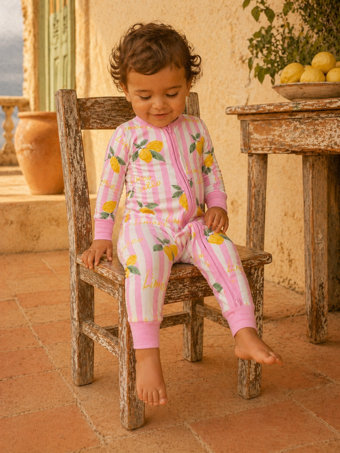 Child in colorful lemon-print pajamas sitting on a rustic wooden chair, outdoors with lemons nearby.