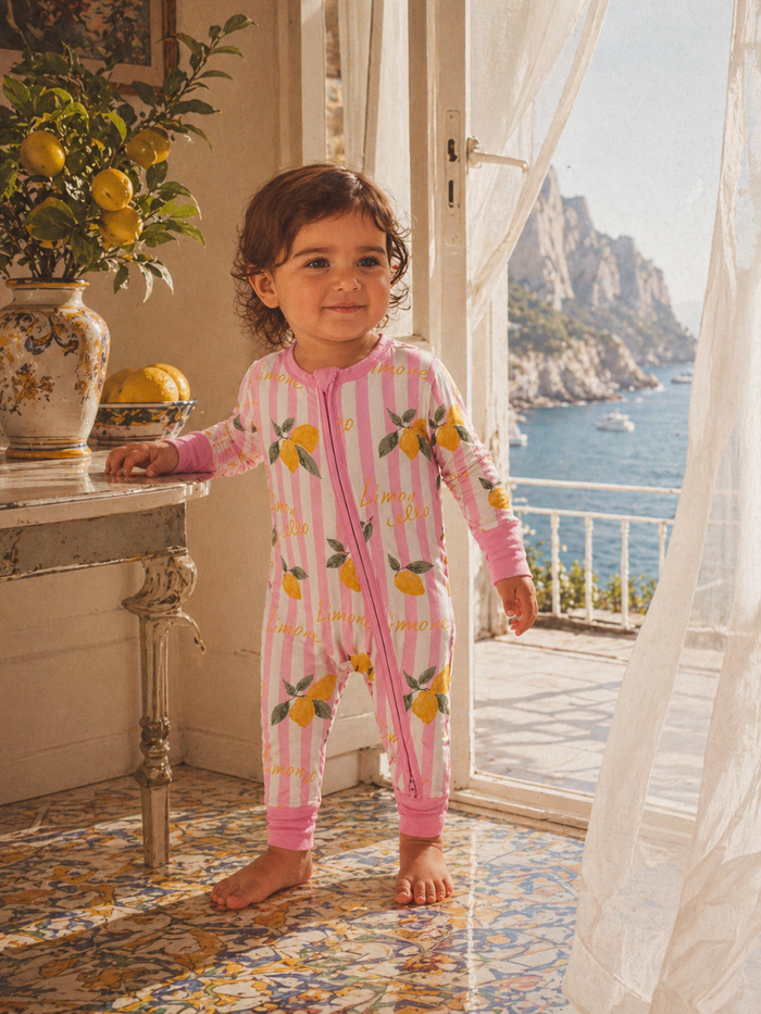 Child in lemon-patterned pajamas standing by a window with coastal view and floral decor.