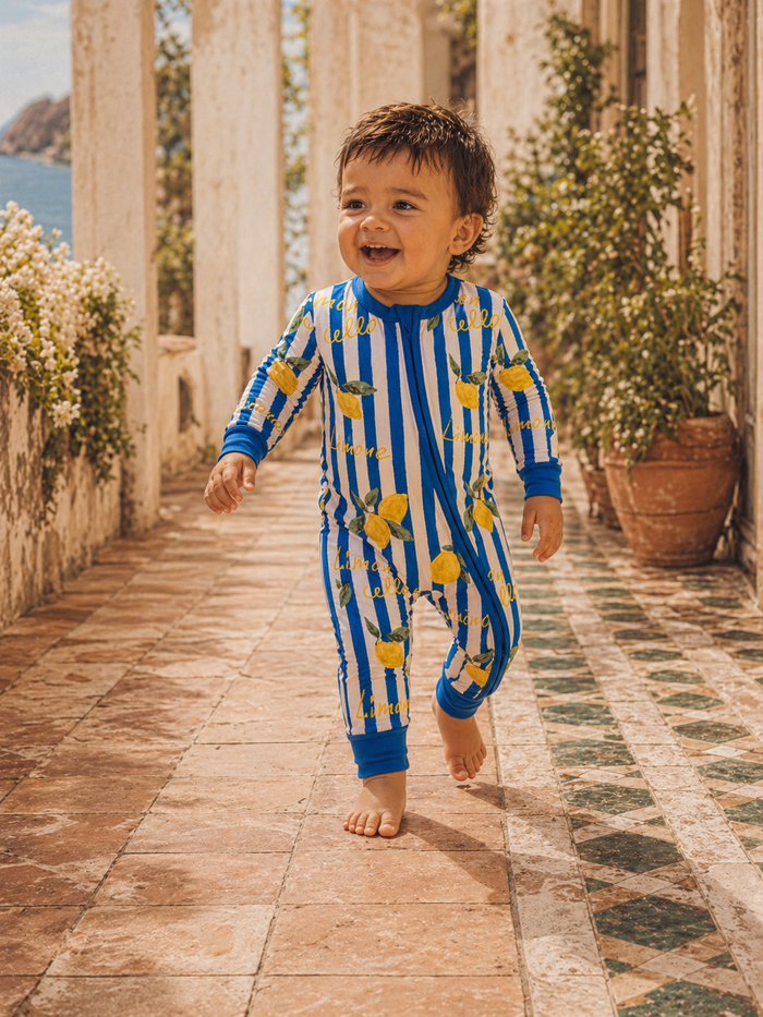 Smiling toddler in colorful lemon-patterned outfit running on a sunny cobblestone path.
