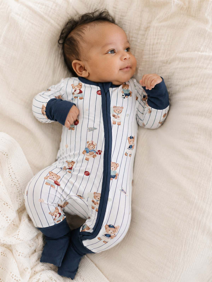 Baby in playful bear-patterned onesie lying on a soft, textured blanket, gazing curiously.