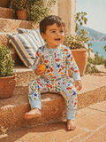 Smiling child in colorful play suit, sitting on stone steps with potted plants and a serene outdoor background.