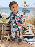 Smiling toddler in a nautical-themed onesie, standing near beach decor, with ocean in the background.