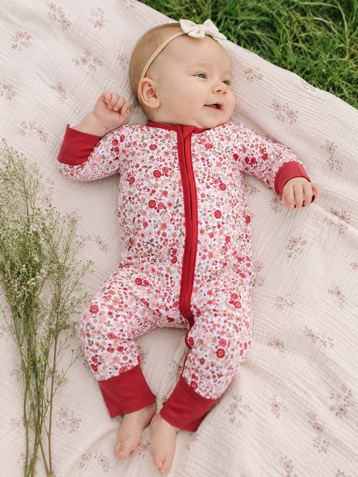 Smiling baby in floral-patterned onesie, lying on a soft blanket with greenery around.
