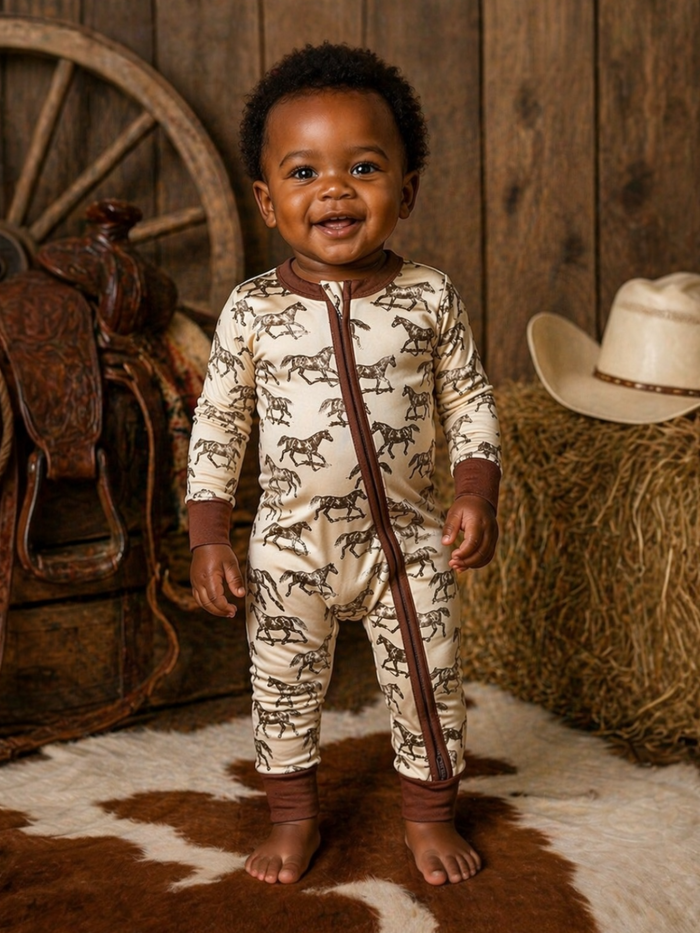 Smiling baby in horse-printed pajamas, standing on a cowhide rug with rustic decor in the background.