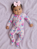 Smiling baby in floral pajamas with a pink bow, lying on a soft purple blanket.