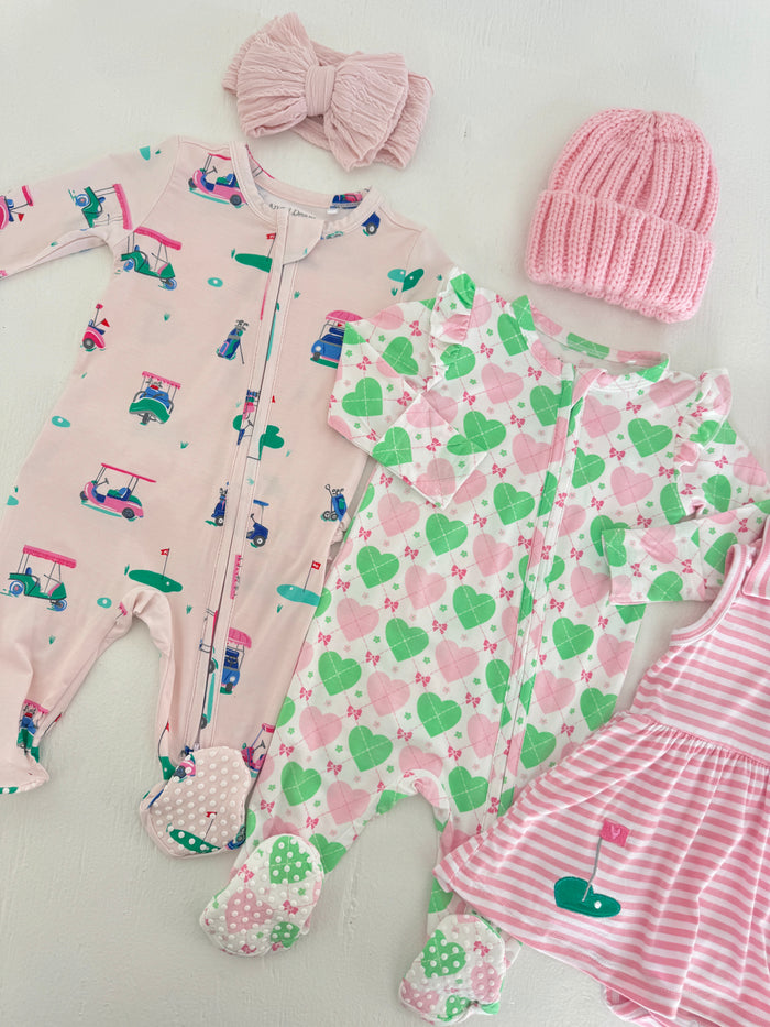 Baby outfits including two zip-up onesies, a pink headband, and a knitted hat, all with playful patterns.