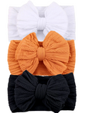Three textured headbands in white, orange, and black with large bow designs stacked vertically.