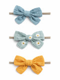 Three colorful fabric hair bows: blue, green with daisies, and yellow, tied on elastic bands.