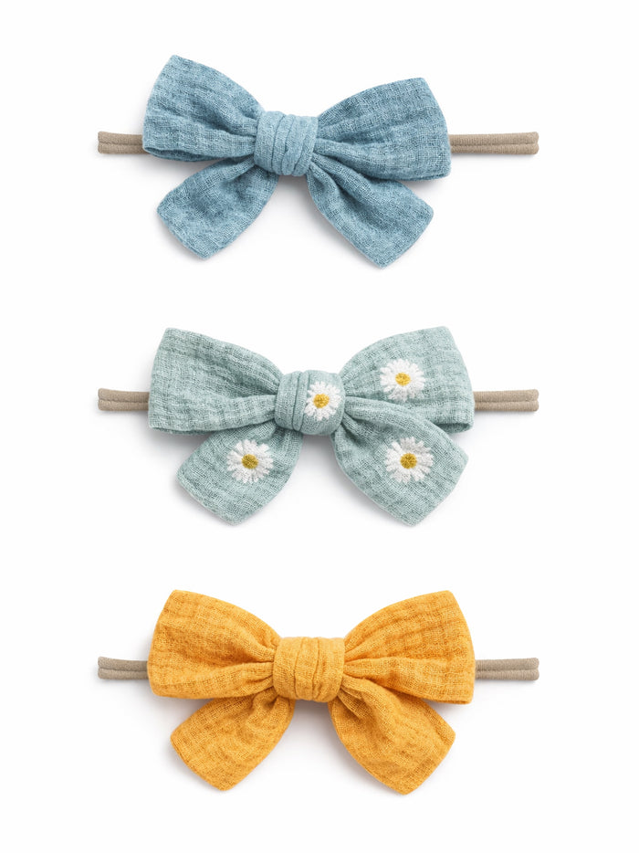 Three colorful fabric hair bows: blue, green with daisies, and yellow, tied on elastic bands.