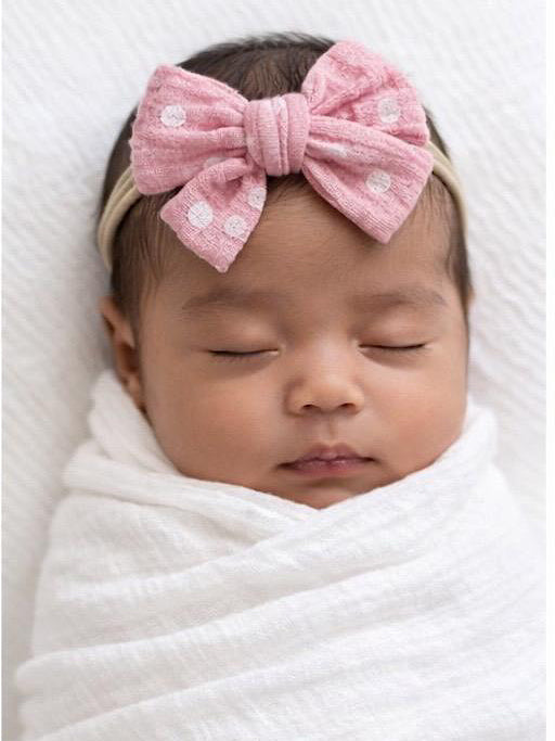 Sleeping baby wrapped in white blanket, wearing a pink polka-dot bow.