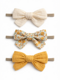 Three colorful fabric hair bows in cream, floral, and mustard on elastic bands.