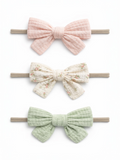 Three hair bows in pink, floral, and green colors on elastic bands against a white background.