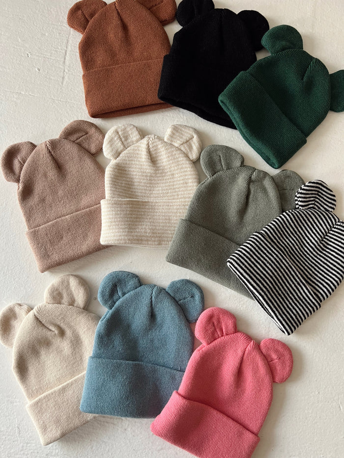 Colorful bear-ear beanies arranged on a light background, showcasing various styles and colors.