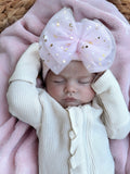 Baby girl sleeping with a large pink bow and white outfit, lying on a pink blanket.
