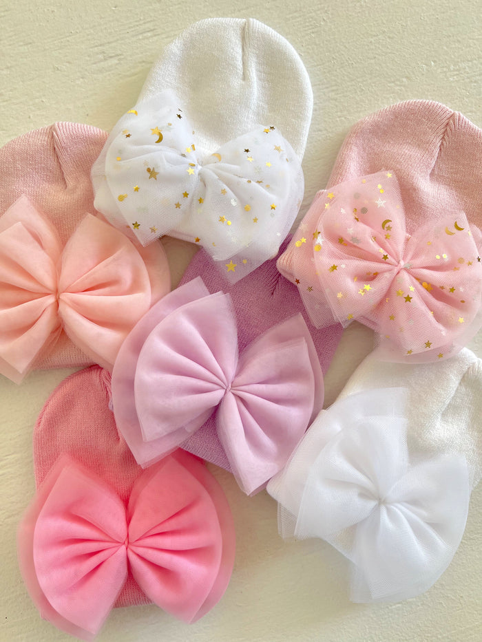 Assorted baby hats with large bows in pink and white, featuring star and moon patterns.