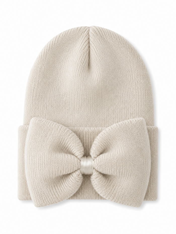 Cream beanie hat with a large bow on the front, perfect for winter fashion.