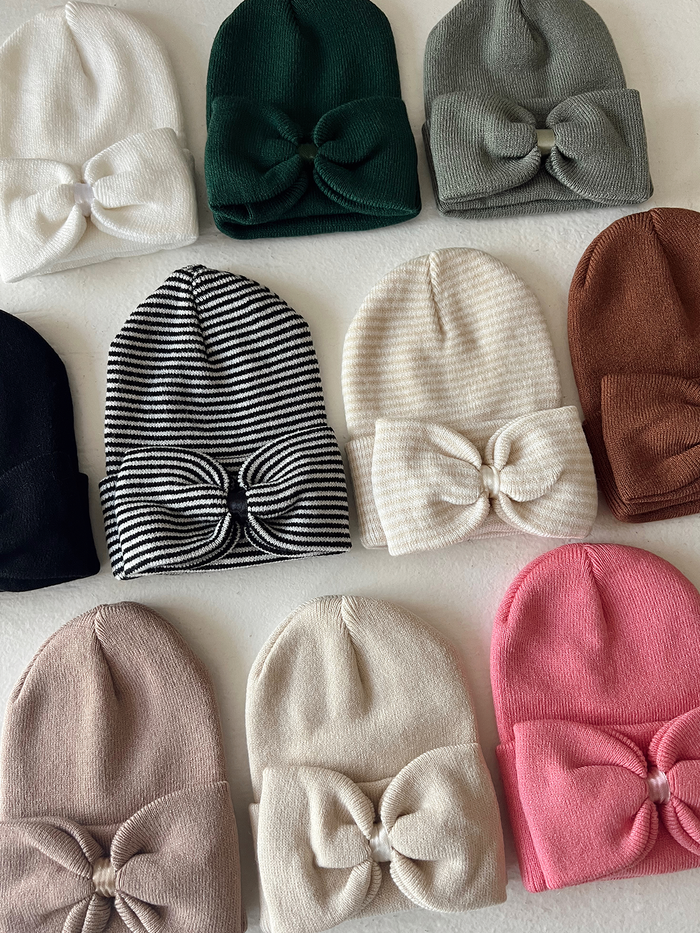 A collection of colorful beanies with bows, arranged neatly on a light background.