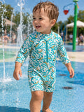 Smiling child in a colorful swimsuit playing in a splash pad, surrounded by water sprays on a sunny day.