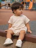 Child with curly hair sits on a playground surface, wearing a striped shirt and white shoes, looking to the side.