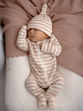 Baby sleeping peacefully in striped pajamas and hat, surrounded by soft, textured fabrics in neutral tones.