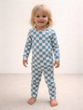 Smiling child in blue and white checkered pajamas standing on a light-colored floor.