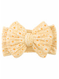 Yellow bow headband with white flowers and orange dots against a plain background. Ideal for stylish accessories.