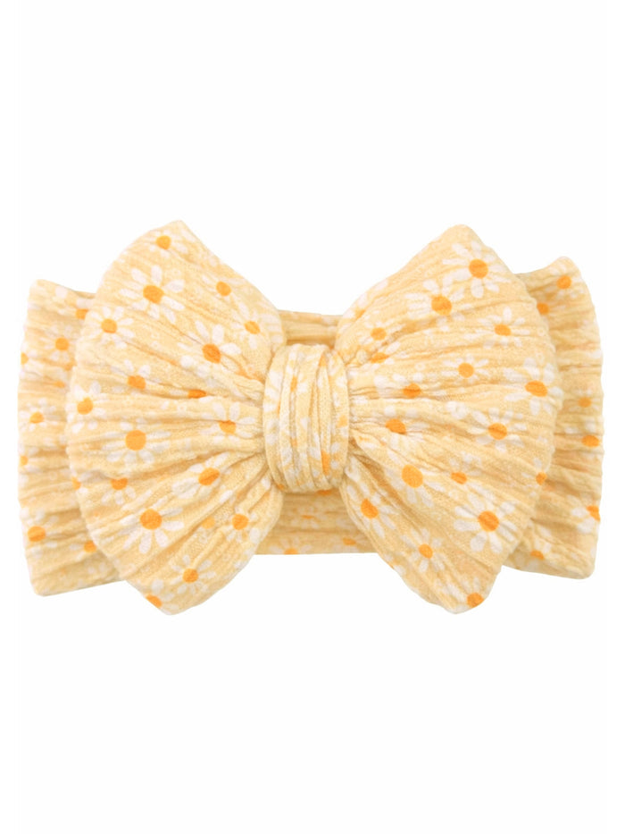 Yellow bow headband with white flowers and orange dots against a plain background. Ideal for stylish accessories.