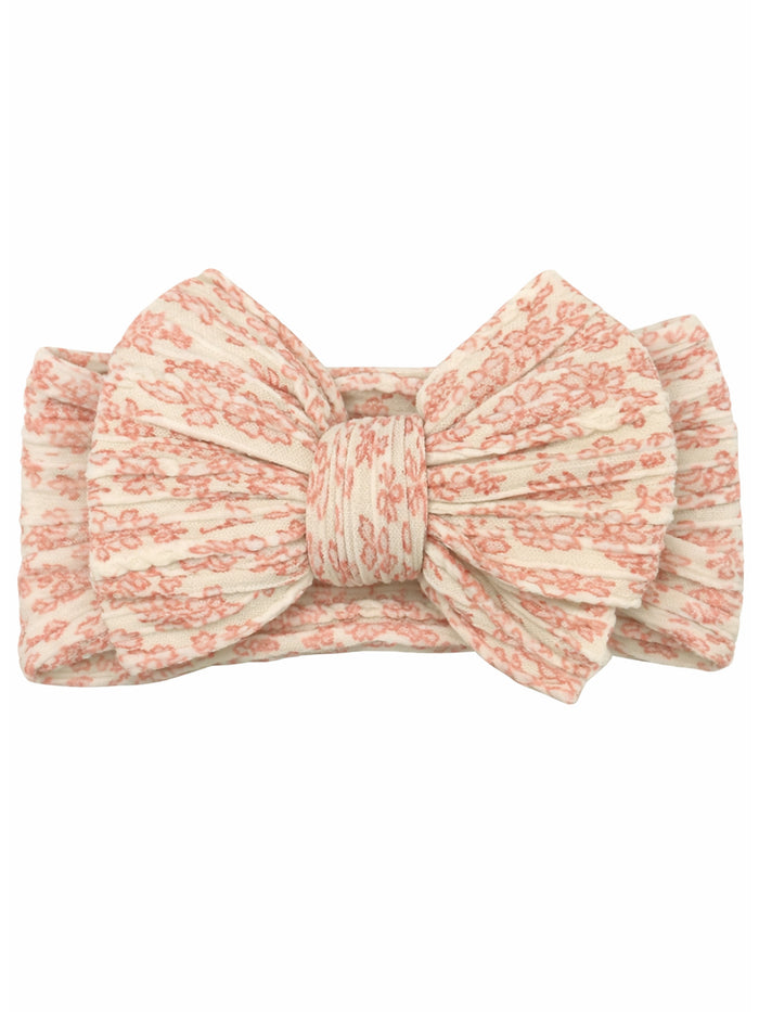 Floral-patterned headband with a large bow in soft peach and cream colors. Ideal for stylish accessories.