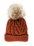 Knitted rust-orange beanie with a plush tan pom-pom on top, featuring a textured cable design.