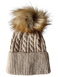 Cable-knit beige beanie with a fluffy, multicolored pom pom on top.