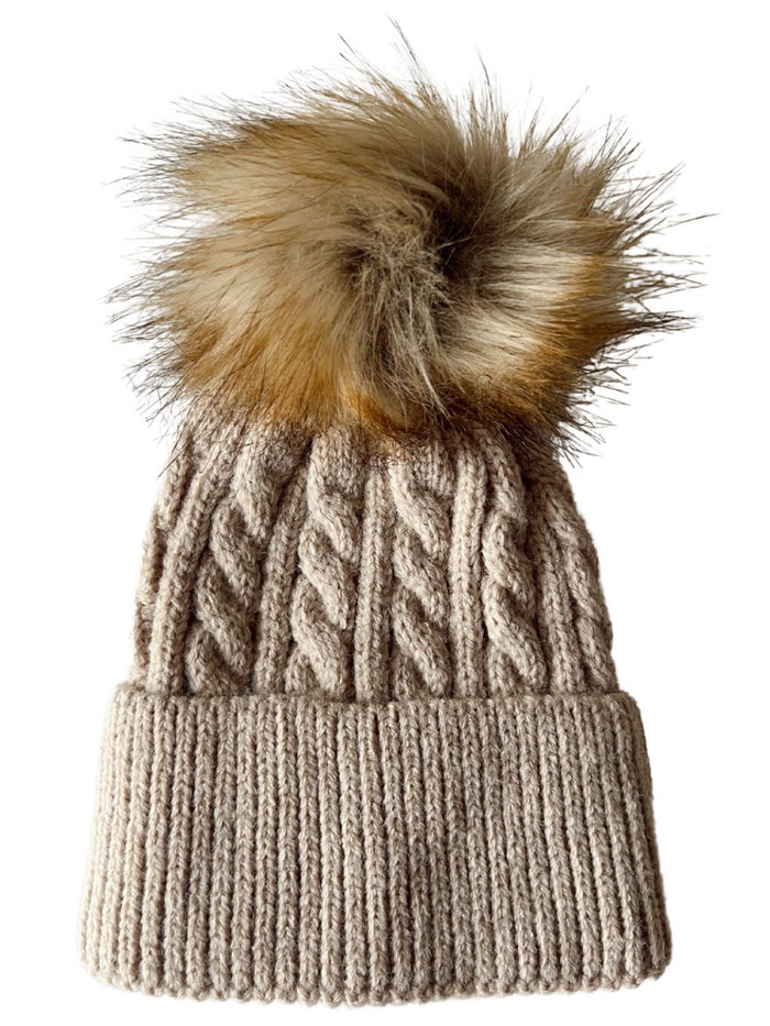 Cable-knit beige beanie with a fluffy, multicolored pom pom on top.